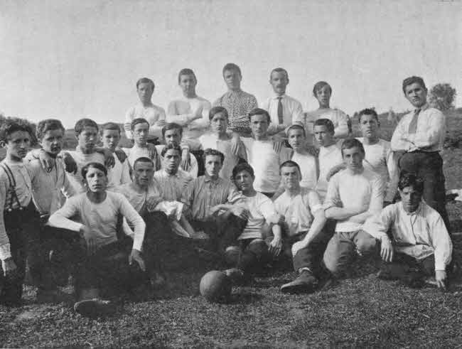 The boys appear to be mostly
teenagers. They are arranged in three rows directly facing the camera, with
the nearest row seated and the back row standing. There is a ball in front
of the boys, and the boys are wearing light tee shirts and dark pants. Two
in the back appear to be older and are wearing shirts with ties. There are
about twenty-five total individuals.