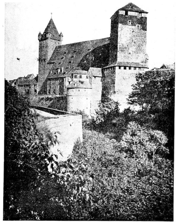 A grainy, vintage black-and-white photograph of a medieval European castle complex, likely the Nuremberg Castle. The structure features a large main building with a steeply pitched roof, a tall square defensive tower, a smaller pointed turret, and stone fortifications rising out of lush foliage in the foreground.