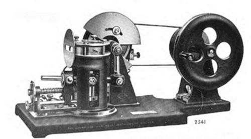 A rotating
cylinder mechanism on a wooden base, connected by belt to a large
four-spoked flywheel.
